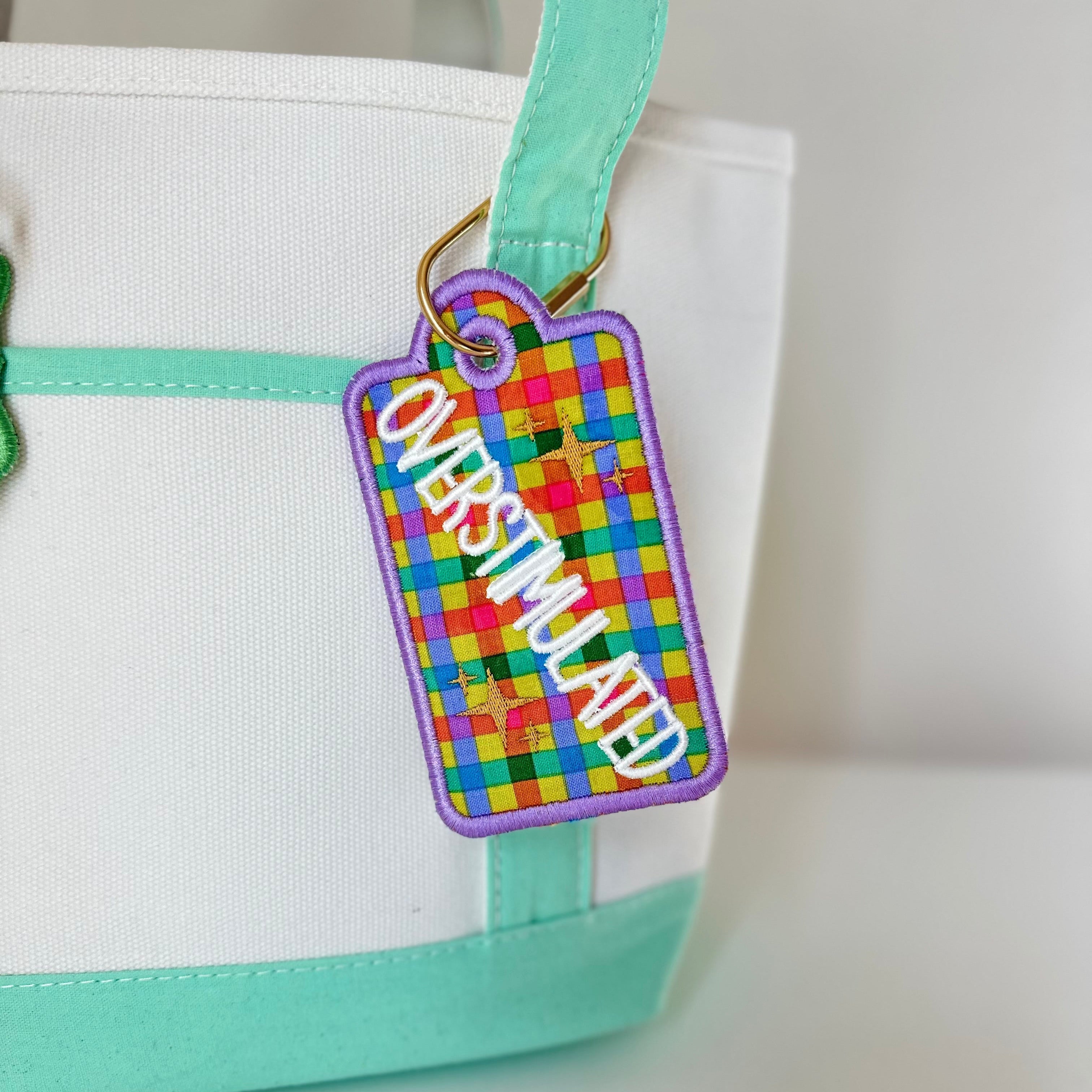 Colorful luggage tag attached to a white bag with green trim on a light gray background