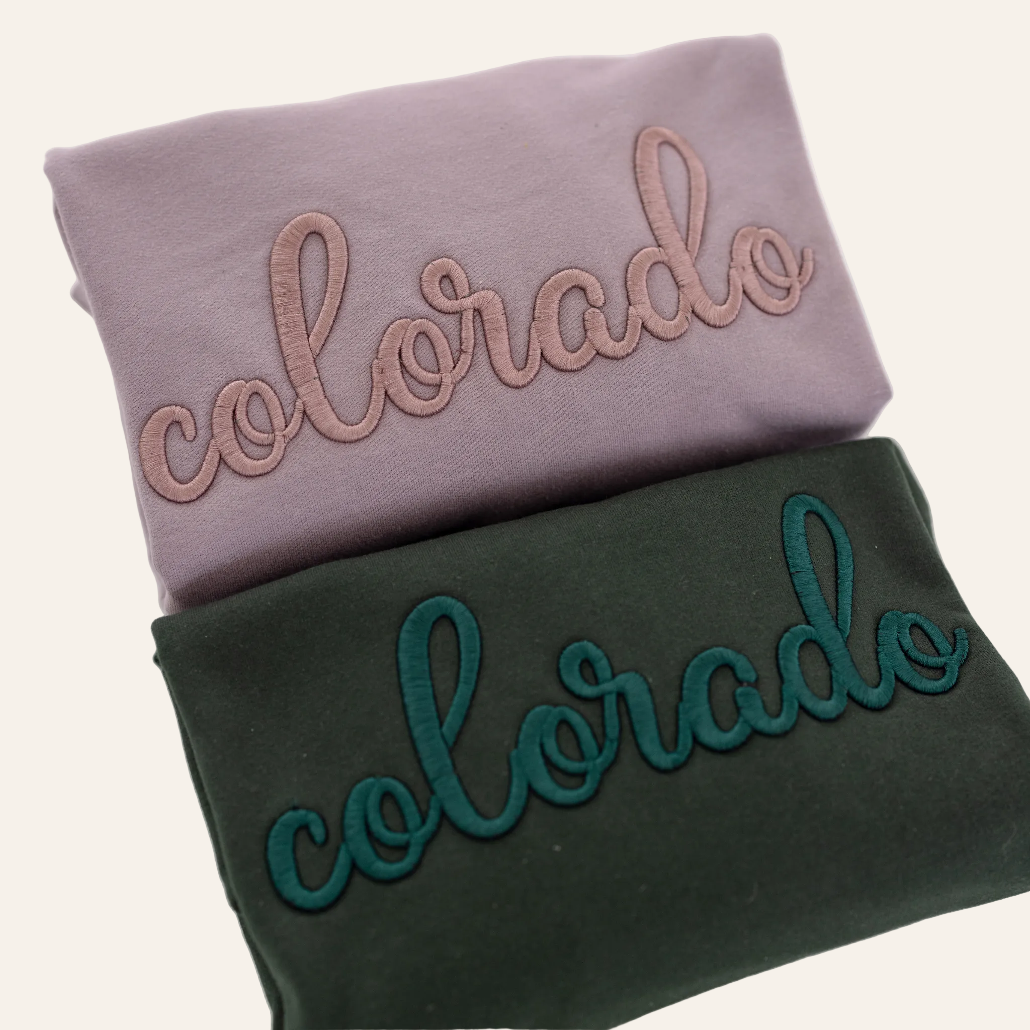 Two folded sweatshirts, one purple and one green, each with the word &