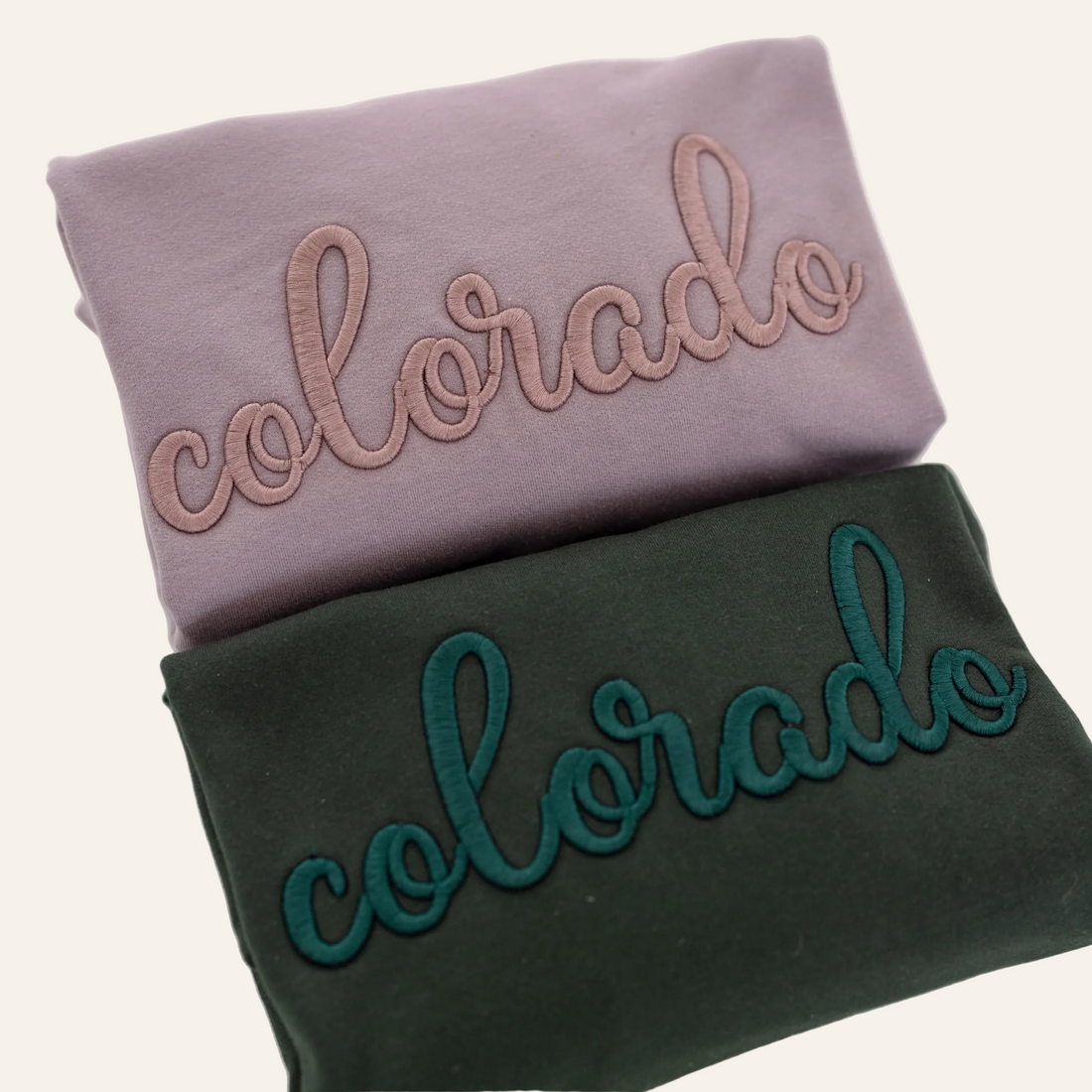 Two folded sweatshirts, one purple and one green, each with the word &