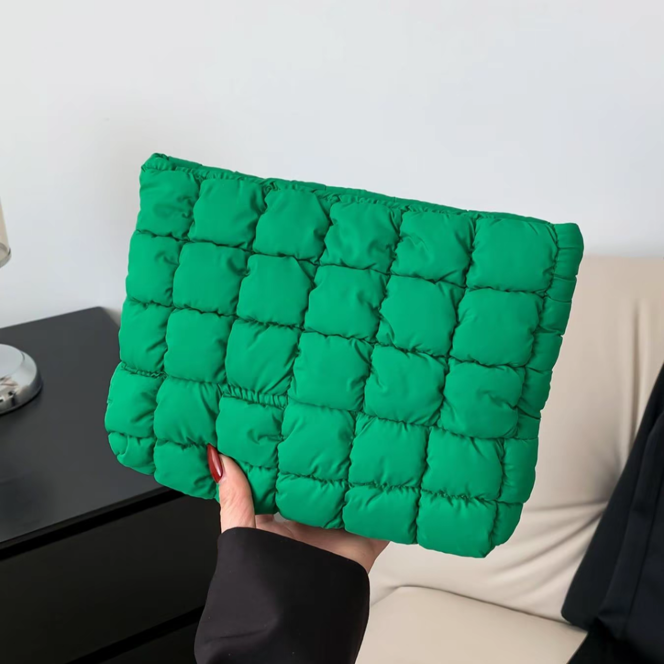 Green quilted clutch held by a person against a neutral background
