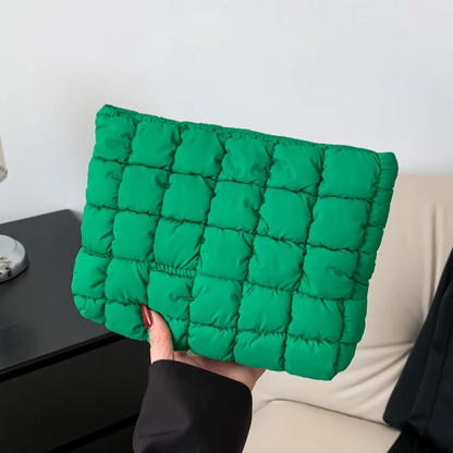 Green quilted clutch held by a person against a neutral background