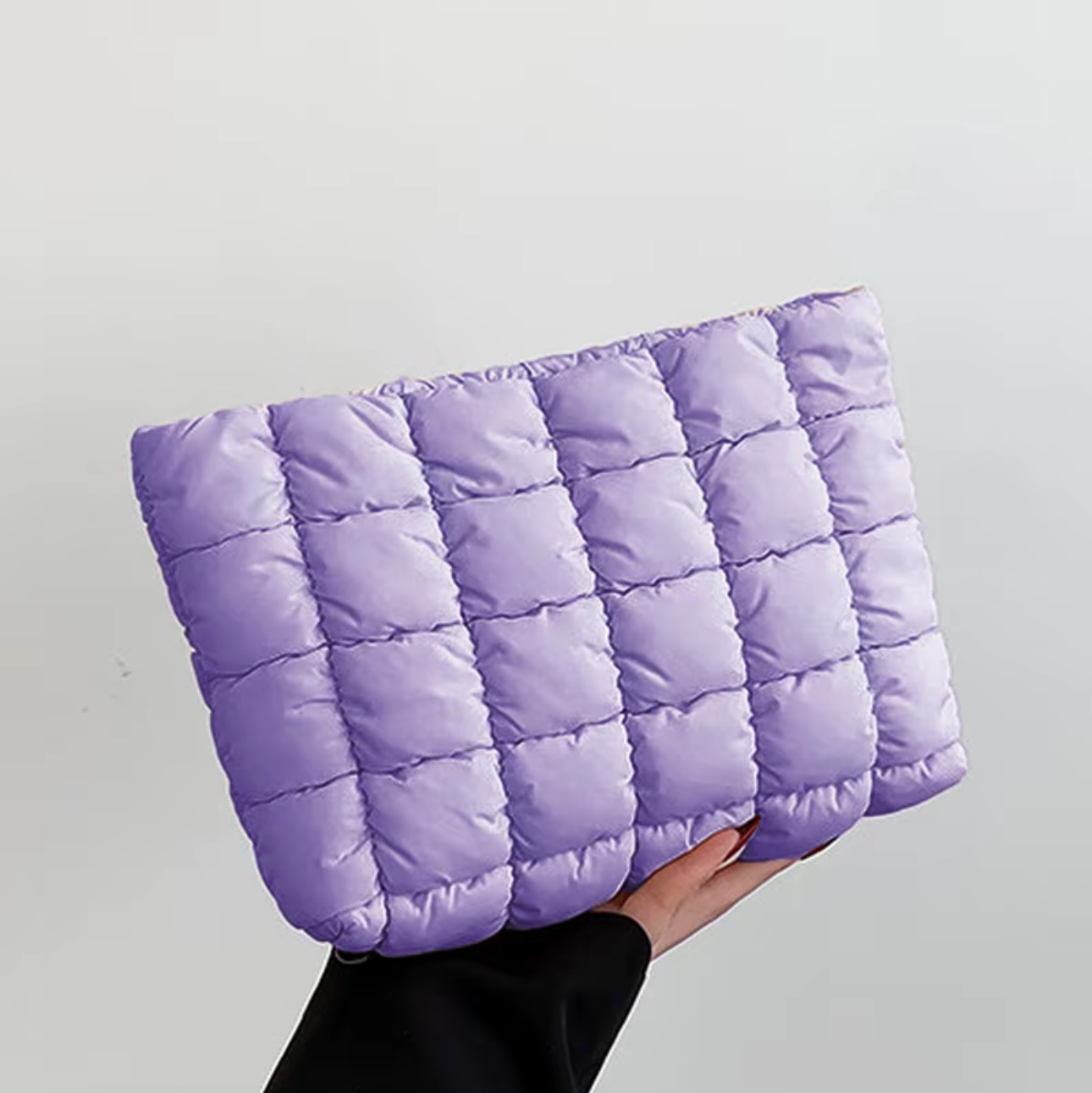 Purple quilted clutch held by a hand against a gray background