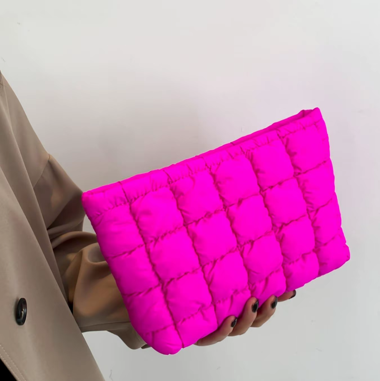 Person holding a bright pink quilted clutch against a plain background