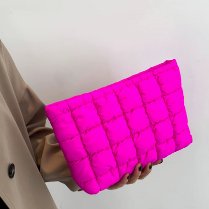 Person holding a bright pink quilted clutch against a plain background